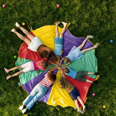 Crianças em círculo deitadas sobre tecido colorido na relva com bolas ao redor