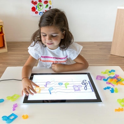 Criança a usar tablet com notas musicais coloridas sobre pautas e notas de plástico coloridas na mesa