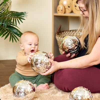 Bebé e mulher com bolas decorativas douradas sentados em tapete dentro de casa