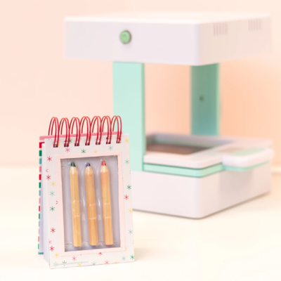 Impressora fotográfica compacta branca e bloco de notas espiralado com lápis coloridos