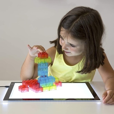 Menina a brincar com blocos de construção translúcidos coloridos sobre uma superfície iluminada