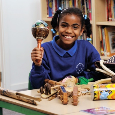 Criança segurando maracá colorido numa mesa com instrumentos musicais tradicionais