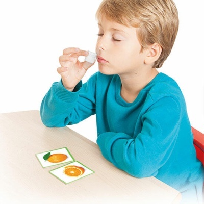 Criança usando conta-gotas junto ao nariz com cartas de frutas na mesa