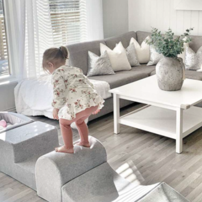 Sala de estar com sofá cinza, mesa de centro branca, vaso com plantas e criança brincando em mobiliário modular cinza.