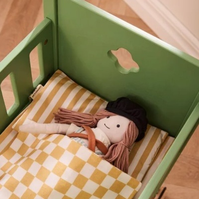 Berço verde com boneca de tecido deitada em cama com roupa de cama amarela às riscas e quadrados