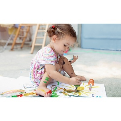 Criança a pintar ao ar livre com tintas coloridas e espátula laranja