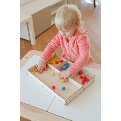 Criança a jogar com bolas coloridas num tabuleiro de madeira