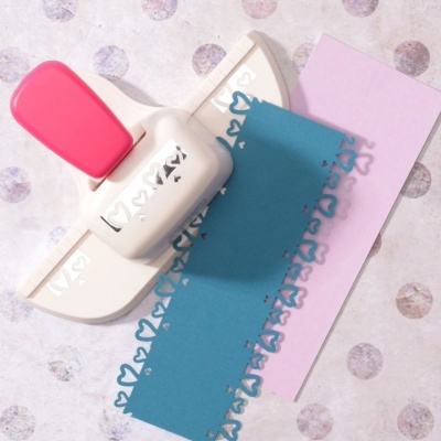 Perfurador de papel branco com alça rosa e recortes decorativos em papel azul e rosa