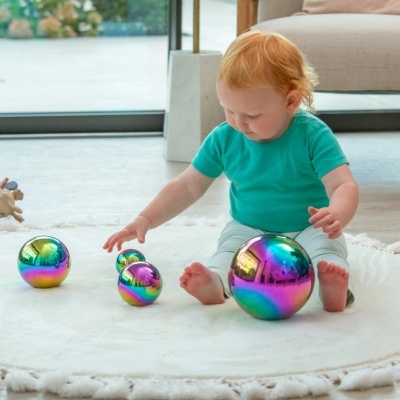 Criança ruiva a brincar com bolas cromadas multicoloridas num tapete branco redondo