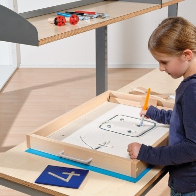 Criança a desenhar num tabuleiro de madeira numa mesa com cartão azul com número 4
