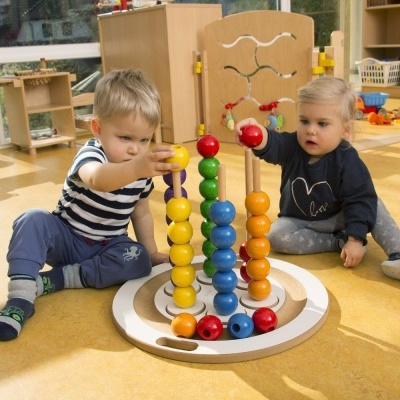 Dois bebés a brincar com brinquedo de madeira colorido no chão de uma sala