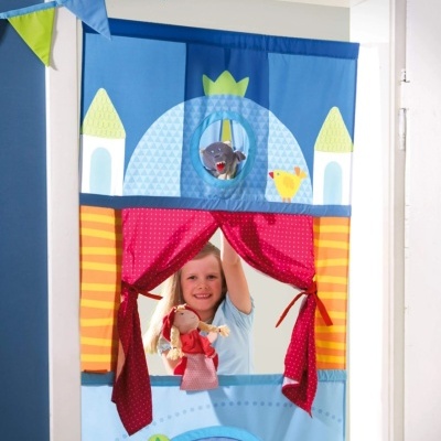 Teatro de fantoches colorido com cortinas vermelhas e castelo azul, menina a brincar.