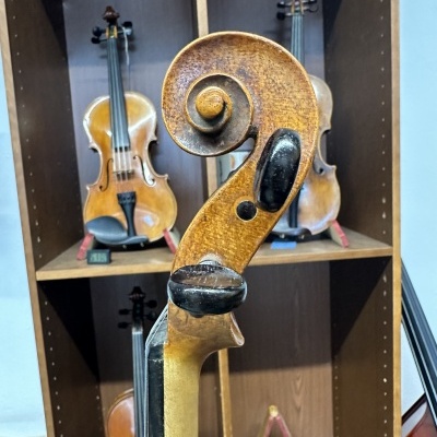 Topete de violino em madeira envelhecida com estante e outros violinos ao fundo