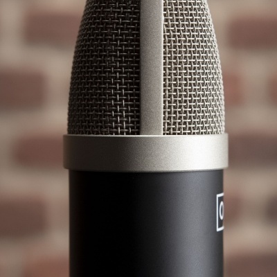 Microfone condensador com grelha metálica prateada e corpo preto fosco
