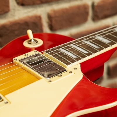 Guitarra elétrica vermelha e amarela com captadores metálicos junto a parede de tijolos