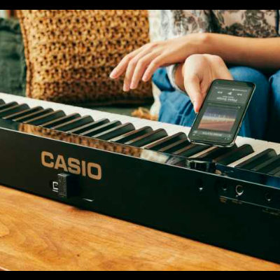 Teclado musical Casio numa mesa de madeira com uma pessoa a segurar um telemóvel