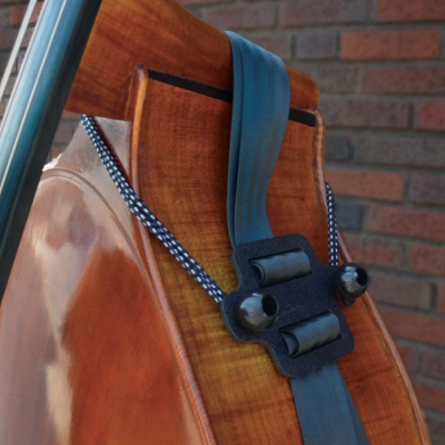 Contrabaixo acústico em madeira com correia cinza e parede de tijolos ao fundo