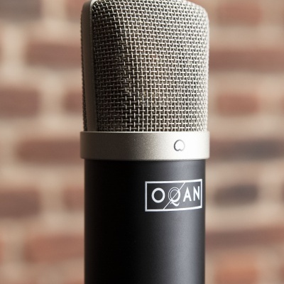 Microfone de estúdio preto com grelha metálica prateada e logo OQAN