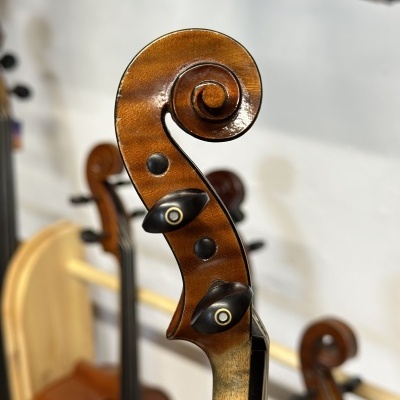 Tampo de madeira de instrumento musical com botões de afinação pretos e fundo desfocado com outros instrumentos