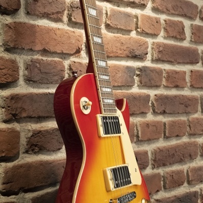 Guitarra elétrica de corpo sólido em gradiente vermelho e amarelo pendurada numa parede de tijolos