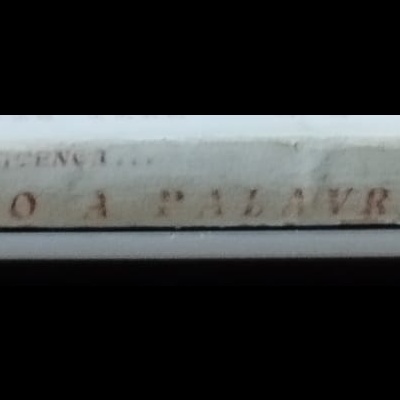 Lombada de livro antigo branca com texto 'PEÇO A PALAVRA!' apoiado sobre portátil prateado