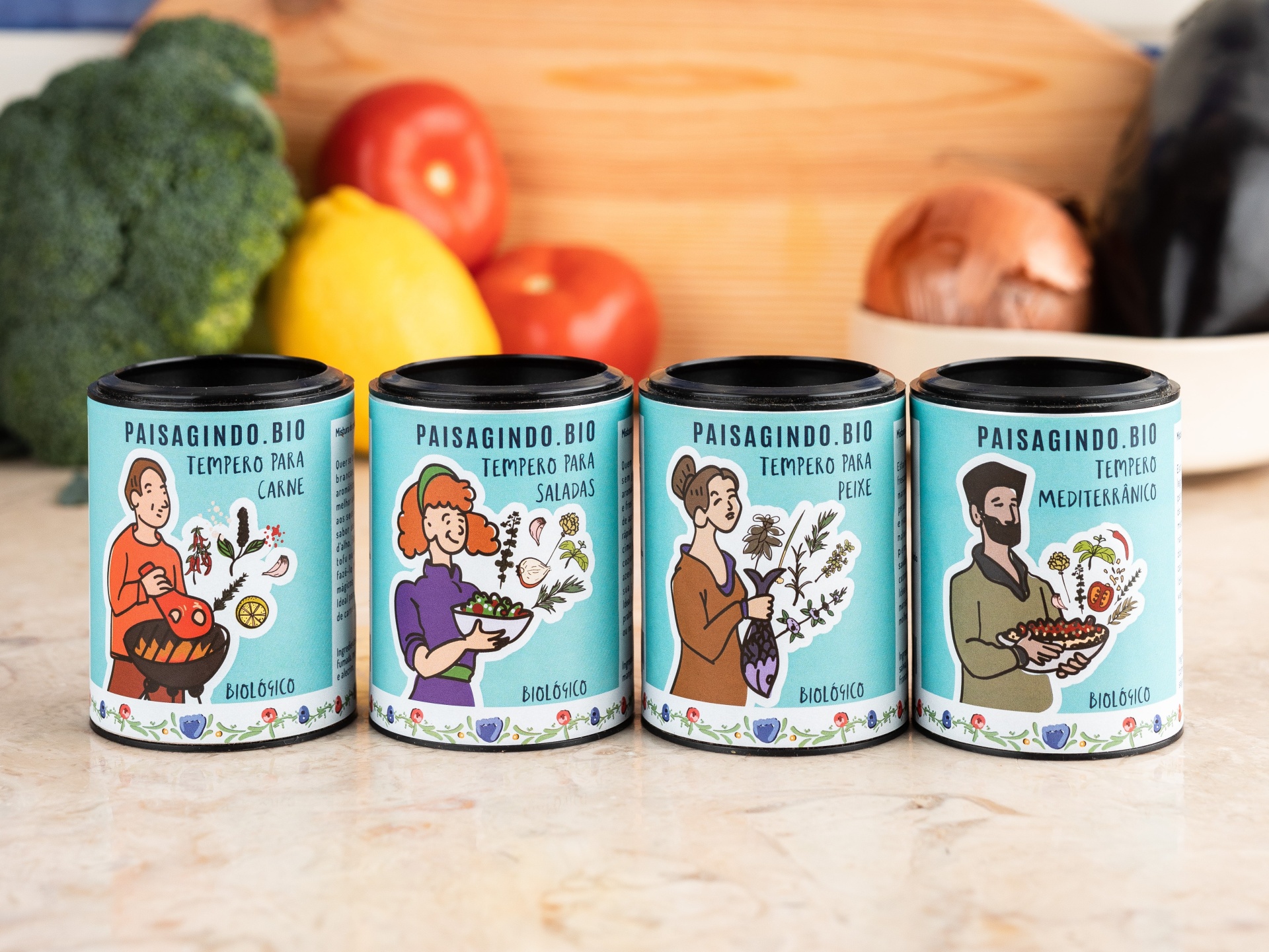 SPICE UP YOUR LIFE | Pack 4 temperos tradicionais Quatro frascos de temperos biológicos PAISAGINDO.BIO para diferentes tipos de comida num balcão com legumes ao fundo