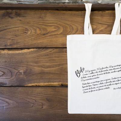 Saco branco com texto impresso pendurado em fundo de madeira rústica