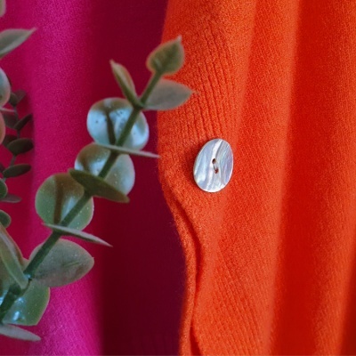 tecidos rosa e laranja com botão branco e folhas verdes em primeiro plano