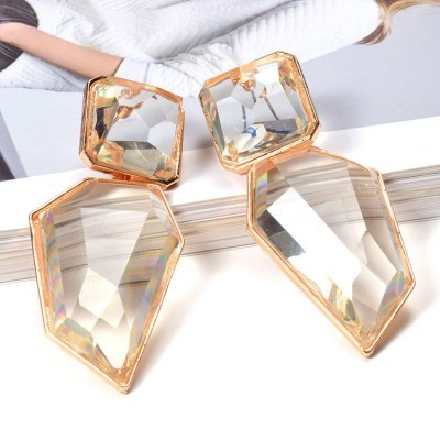 Brincos geométricos de cristal transparente com moldura dourada sobre livro aberto