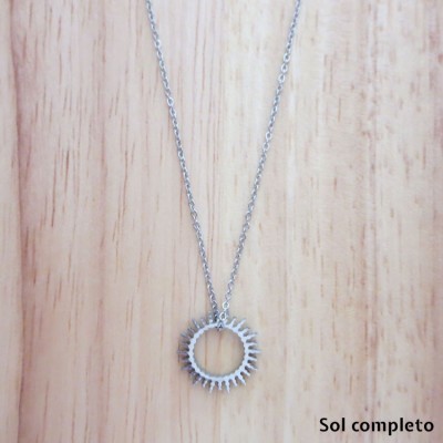 Colar em metal prateado com pendente circular e padrão de picos sobre madeira clara