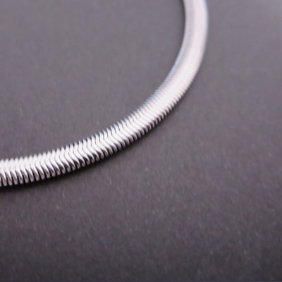 Colar fino de metal prateado com textura em ziguezague sobre superfície preta