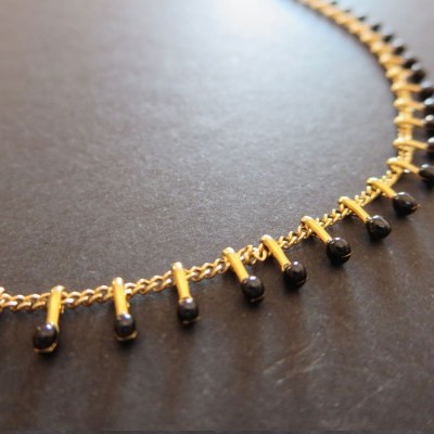 Colar dourado com pingentes pretos na superfície escura