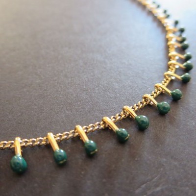 Colar dourado com contas verdes penduradas sobre fundo cinzento