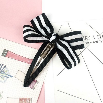 Presa de cabelo riscada preta e branca com laço em fundo de papéis coloridos