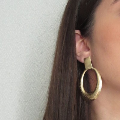 Brincos ovalados em ouro numa orelha feminina
