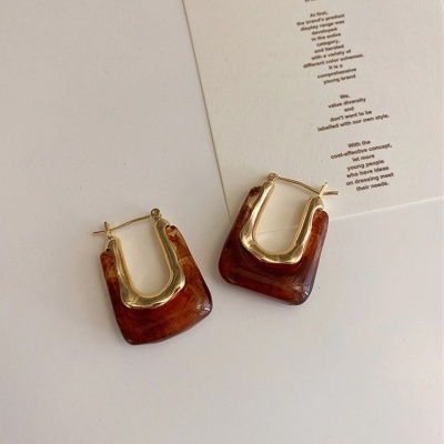 Brincos castanho e dourado sobre fundo branco com papel impresso