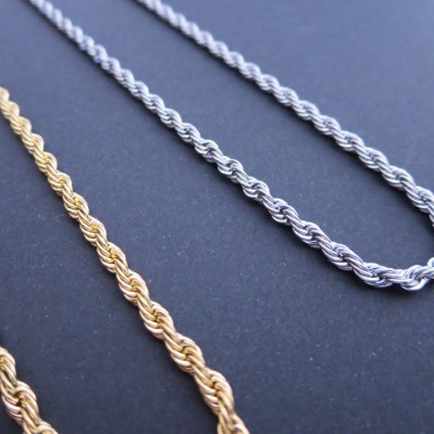 Três colares tipo corda torcidos em dourado e prata sobre fundo escuro