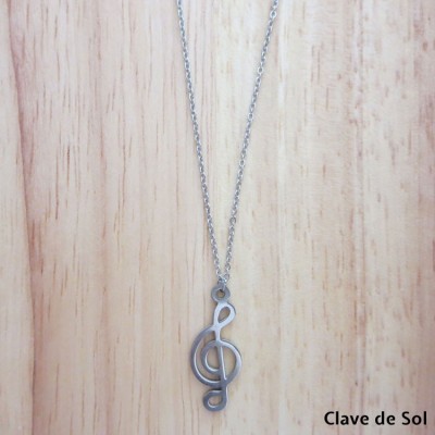 Colar prateado com pendente de clave de sol sobre fundo de madeira clara