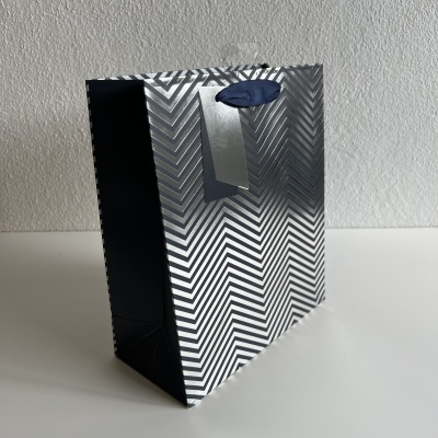 Saco de presente em papel preto e prata com padrão ziguezague e alça azul escura