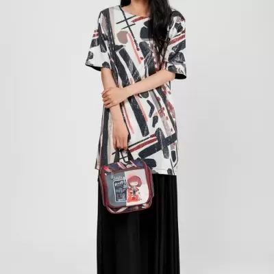 Mulher com túnica estampada e vestido preto segurando mala vermelha e preta