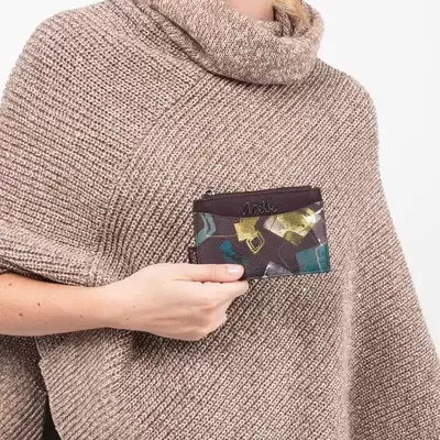 Carteira pequena colorida com detalhe em couro castanho segurada por mulher com capa de malha castanha clara