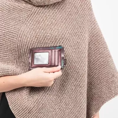 Carteira pequena castanha em couro com visor transparente, segurada por mulher com capa bege de malha