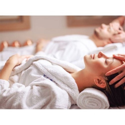 Duas pessoas deitadas com roupões brancos a receber massagem na cabeça num spa