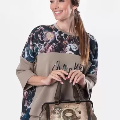 Mulher com blusa estampada azul e bege, calças bege e bolsa de mão com ilustração e texto