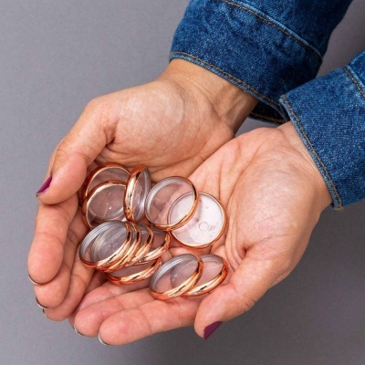 Mãos segurando objetos redondos transparentes com bordas metálicas cor de cobre.