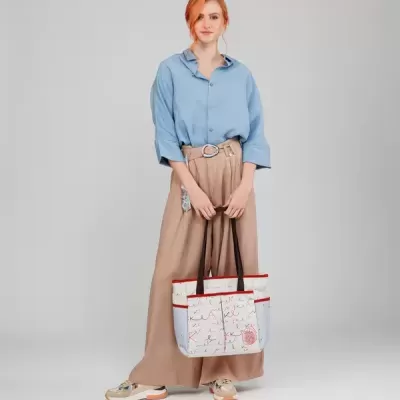 Mulher com camisa azul, calças bege largas e mala branca decorada