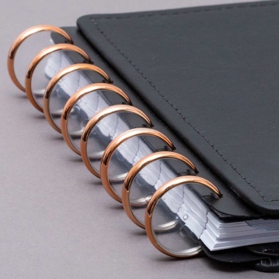 Caderno preto com argolas metálicas cor cobre e folhas brancas