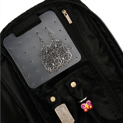 Porta-joias preto aberto mostrando brincos prateados pendurados e acessórios com detalhes coloridos.