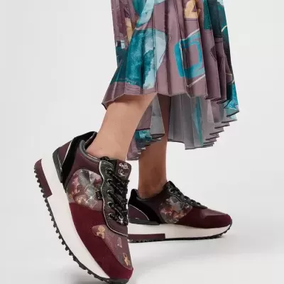 Ténis desportivos bordô com padrão floral e sola branca sob saia plissada multicolorida