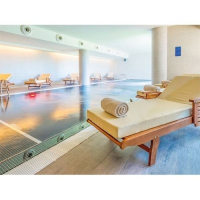 Piscina interior com espreguiçadeiras de madeira e almofadas brancas